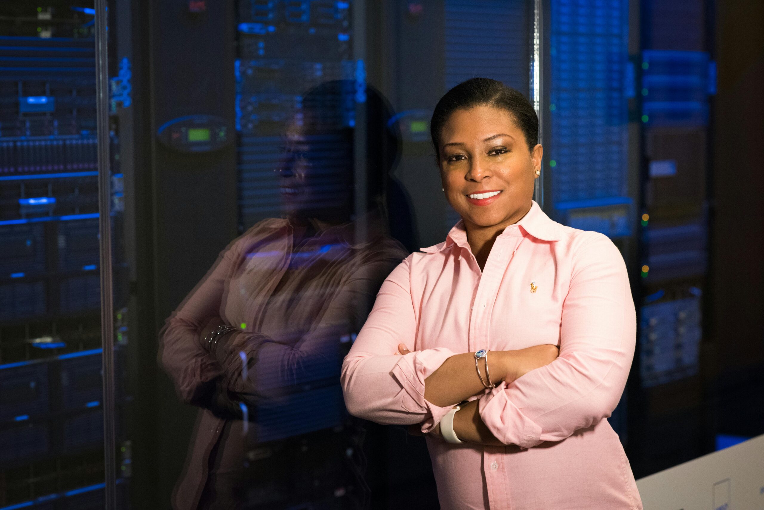 Smiling IT professional with crossed arms in a server room, reflecting her expertise.